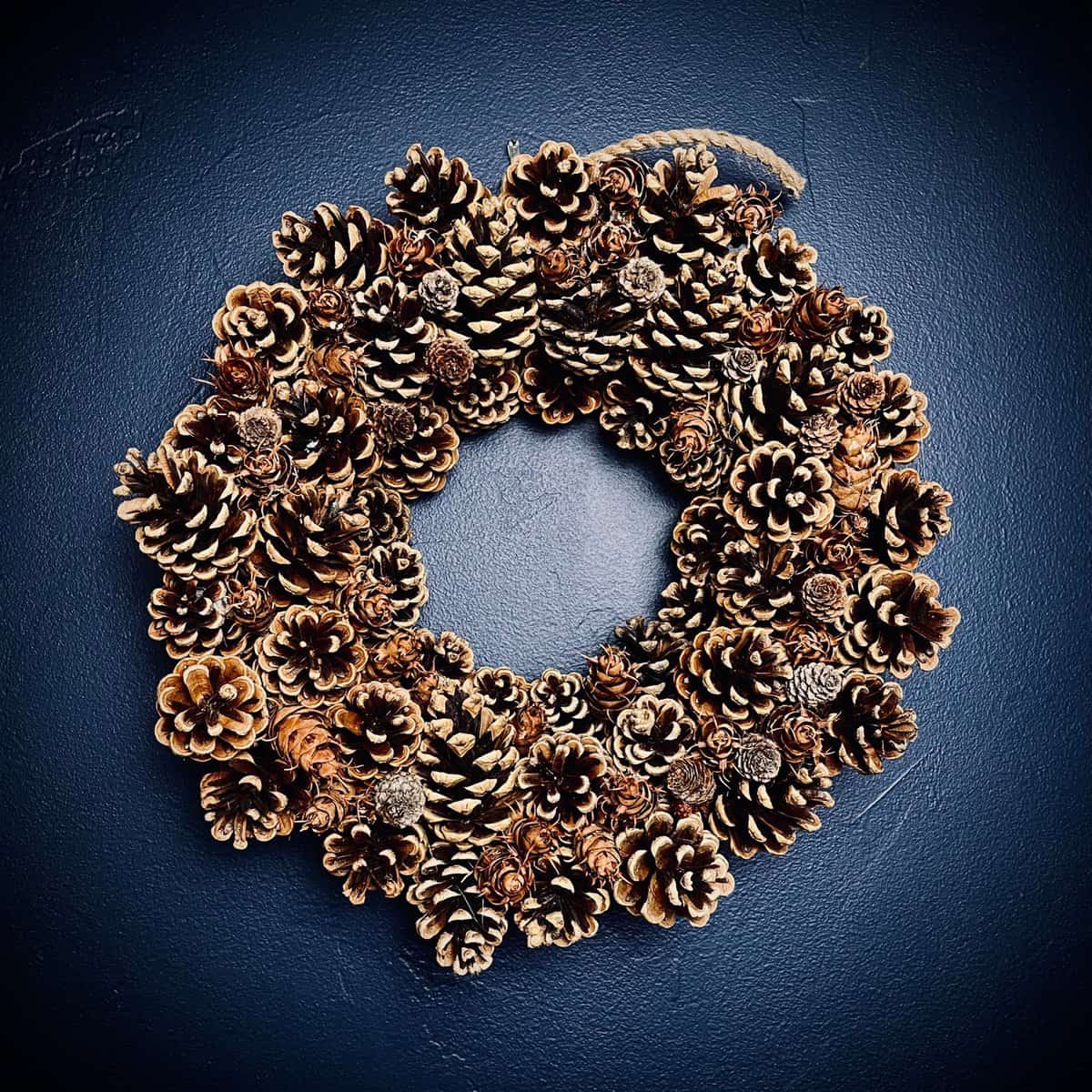 DIY Pinecone Wreath hanging against a navy blue wall.