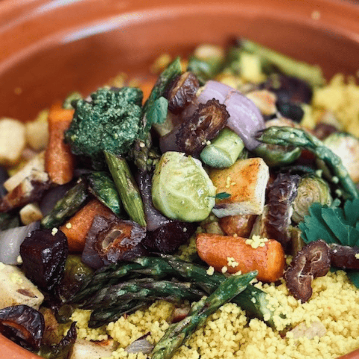 Vegan couscous with roasted vegetables and a mint pesto in a terracotta dish.