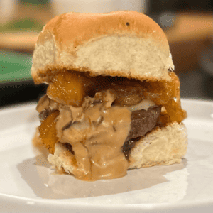 Cheeseburger slider with candied pineapple and jalapeños sitting on a white plate.
