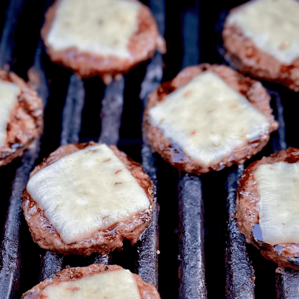 Cheeseburger slider patties on a grill.