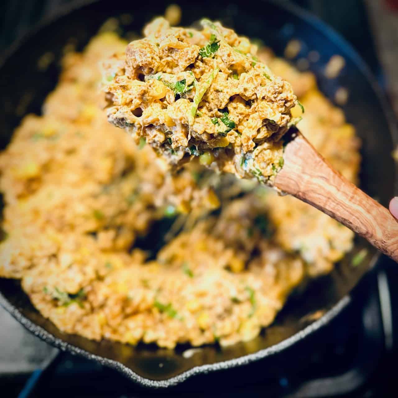 Chorizo filling in a cast iron skillet and a wooden spoon holding some in the foreground.