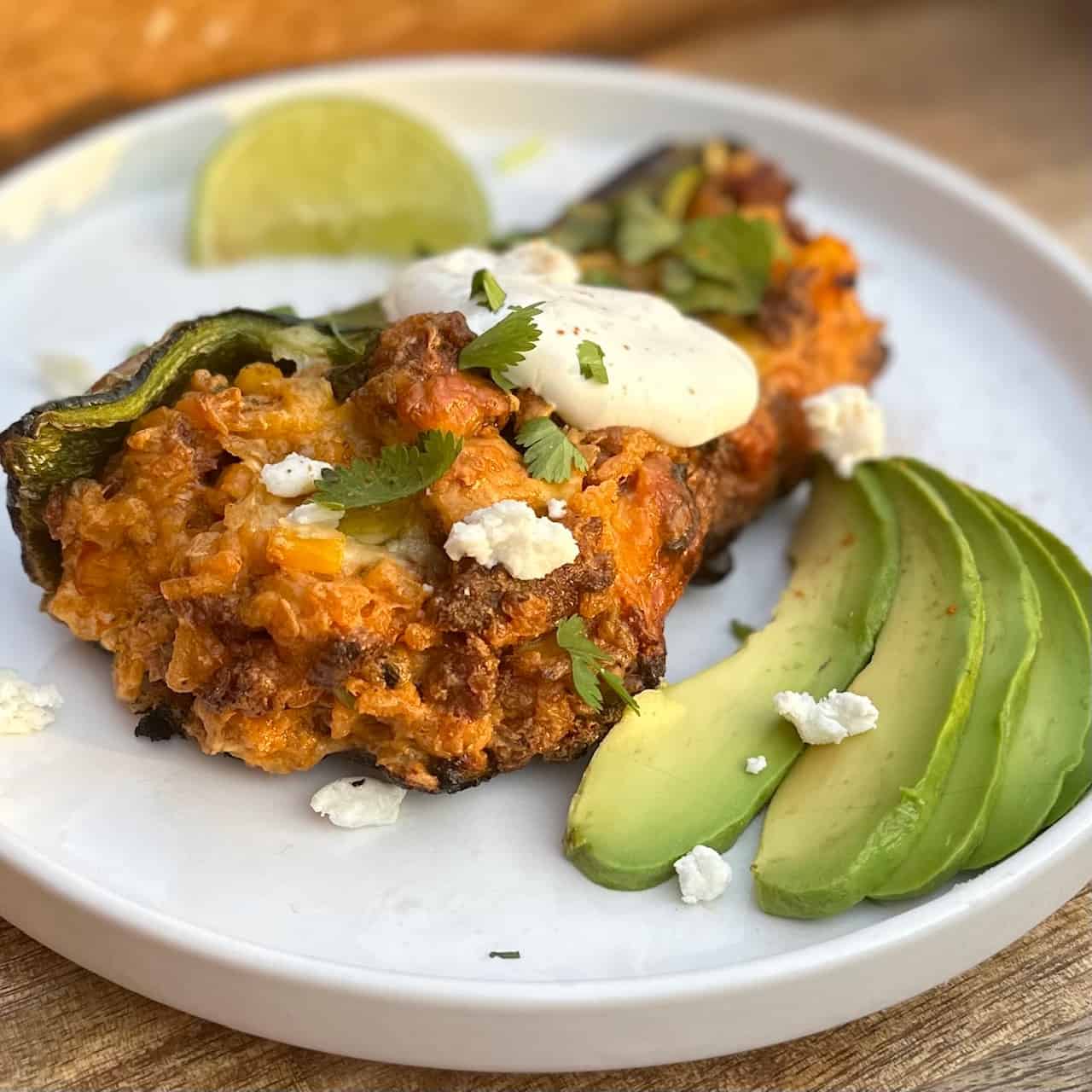 White plate with Mexican stuffed pepper, garnished with avocado and lime wedge.