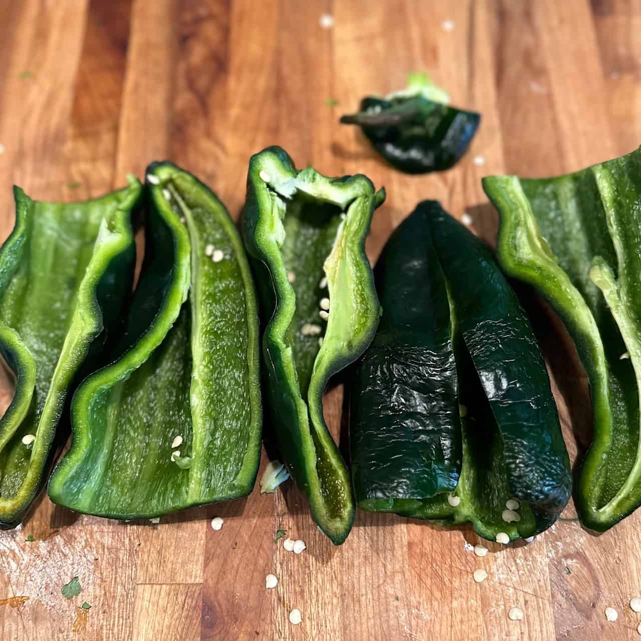 Peppers cut in half and layed out on a wooden cutting board.