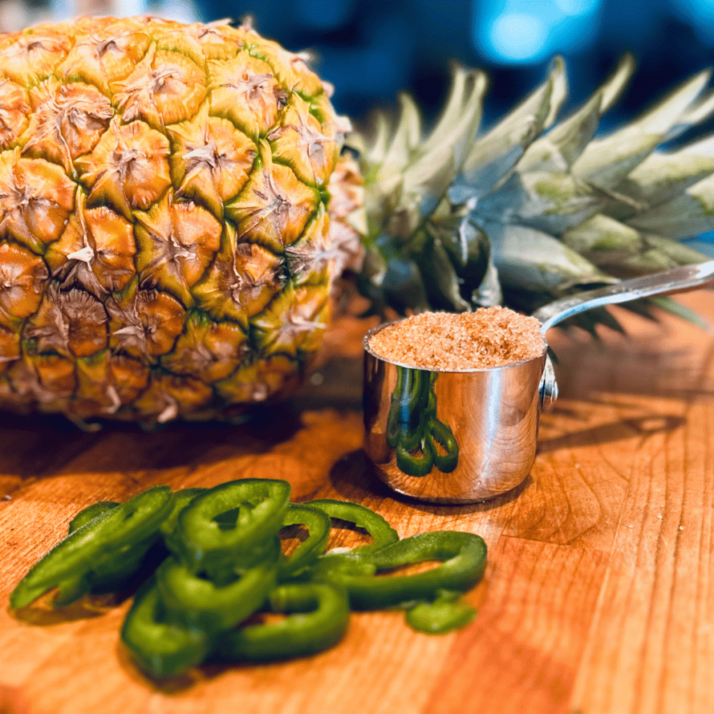 Fresh pineapple, sliced jalapeños and brown sugar sitting on a wooden cutting board.