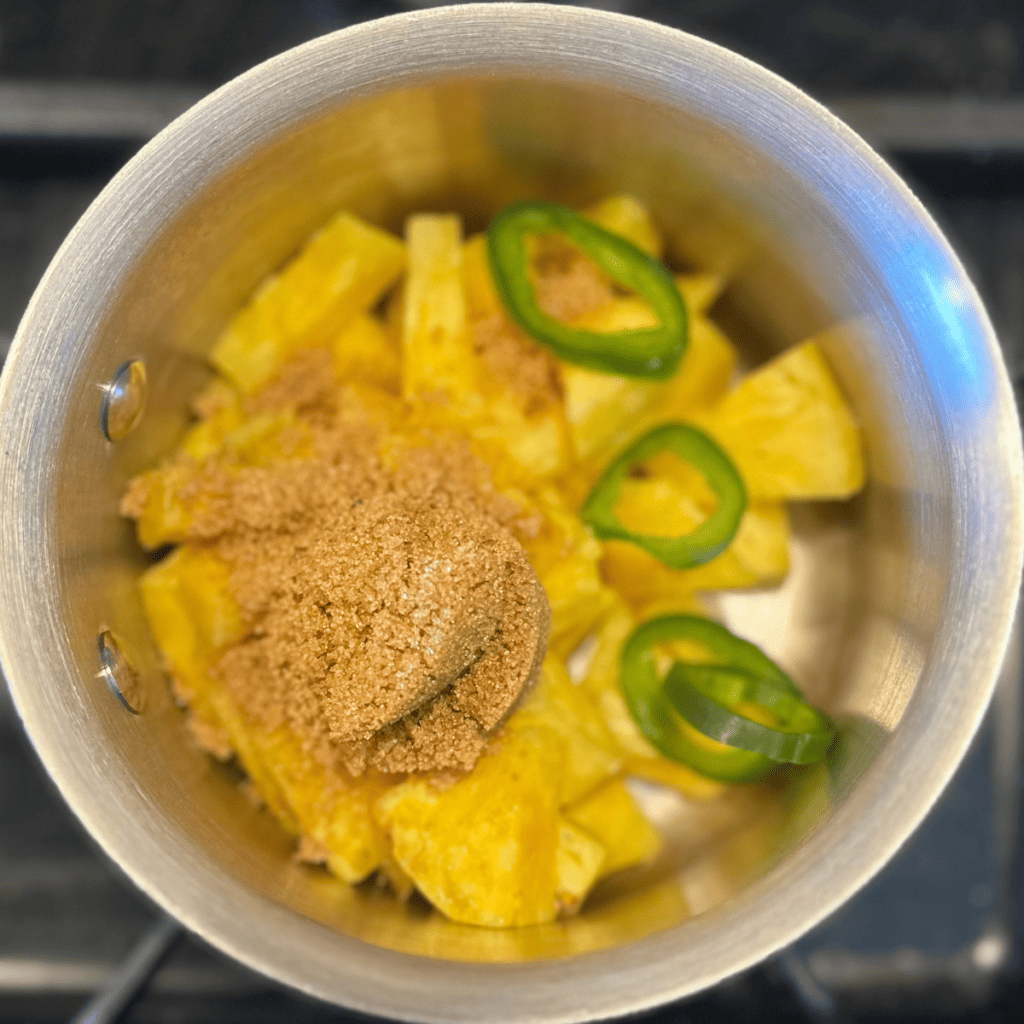 Pot with pineapple chunks, sliced jalapeño and brown sugar.