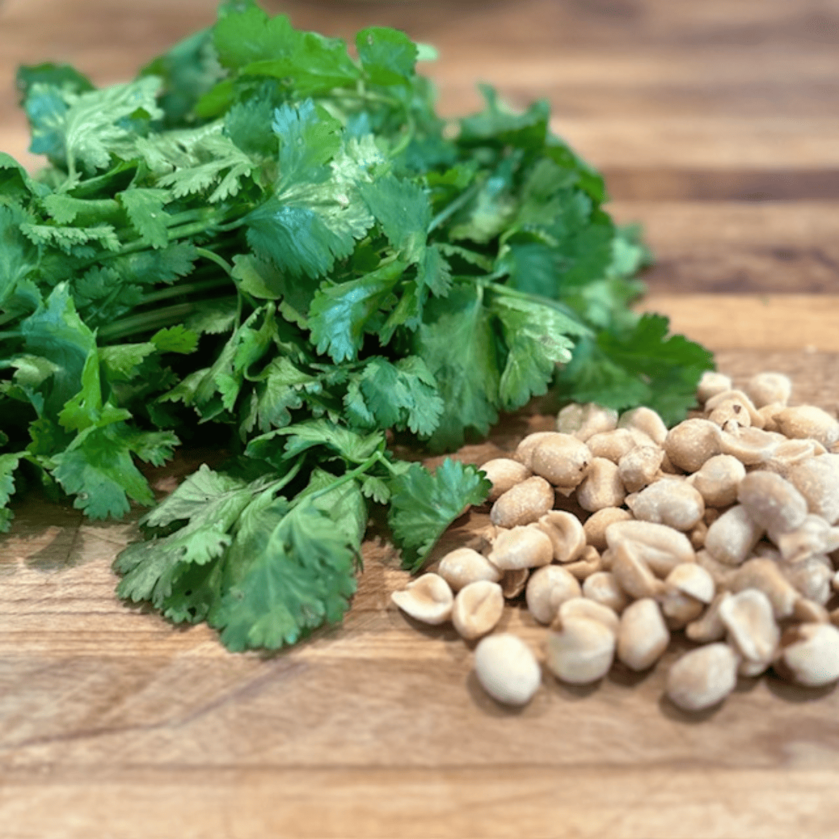 Chopped cilantro and peanuts sitting on a wooden cutting board.