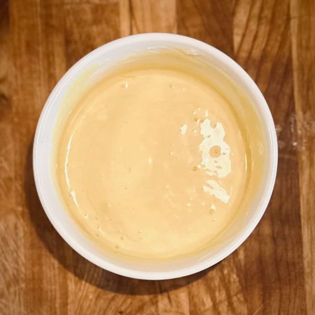 White ramekin filled with honey mustard sauce, sitting on a wooden cutting board.