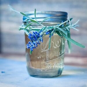 Glass mason jar filled with lavender simple syrup and tied with a sprig of lavender around the top.