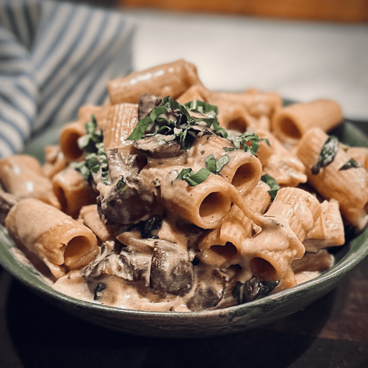 Bowl of Creamy Mushroom Rigatoni on a dark wood cutting board.