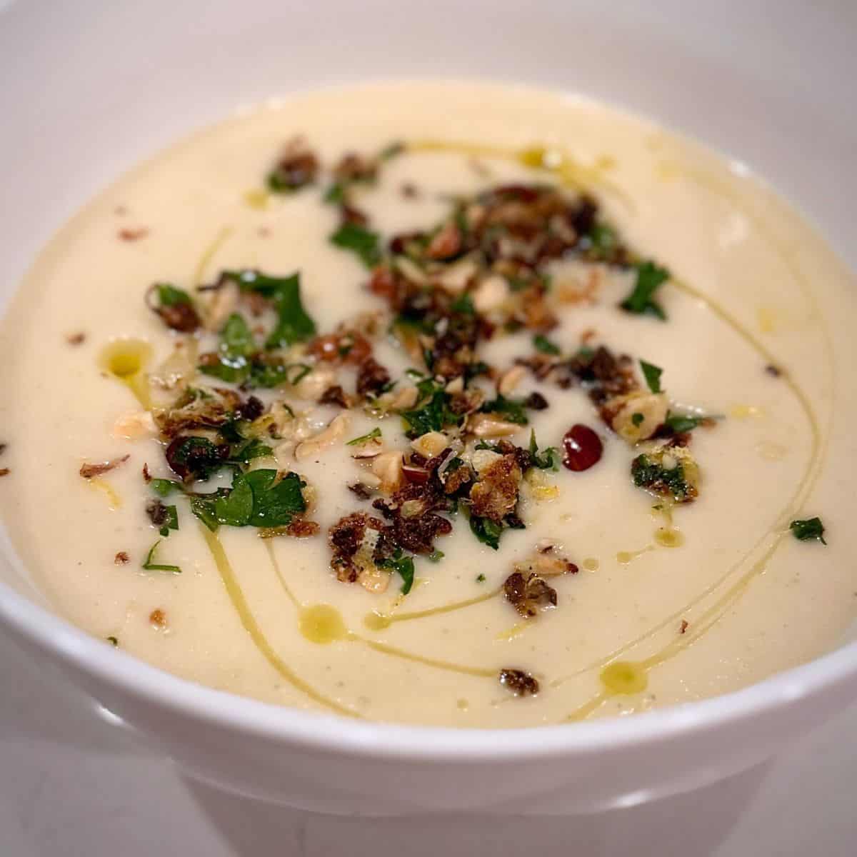 White bowl of Cauliflower soup with lemony hazelnut topping.