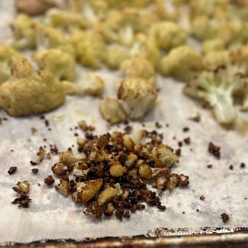 Tiny brown bits of cauliflower on a baking sheet.