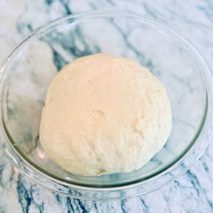 Cottage cheese bread dough proofing in a glass bowl.