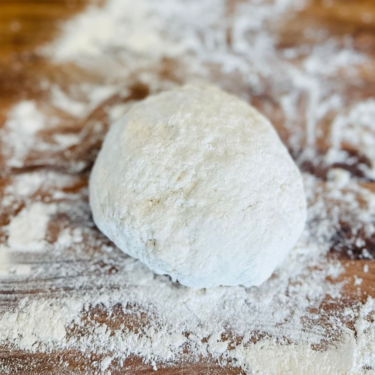 Ball of fry bread dough on a floured wooden cutting board.