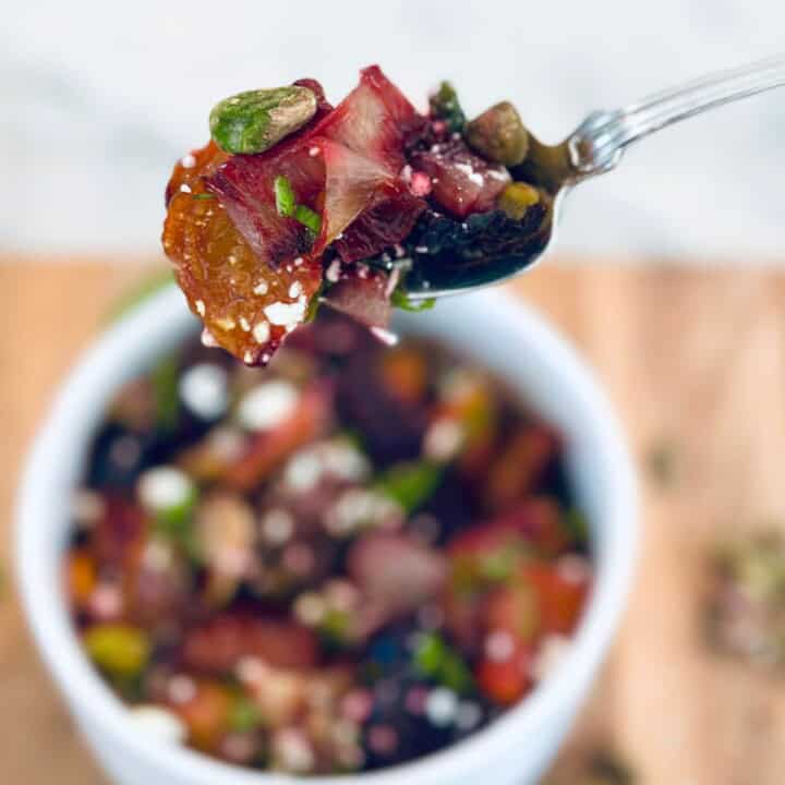Roasted vegetable salad on a fork, held over a white bowl of salad.