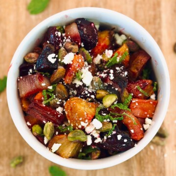 Birds eye view of a roasted vegetable salad in a white bowl on a wooden surface.