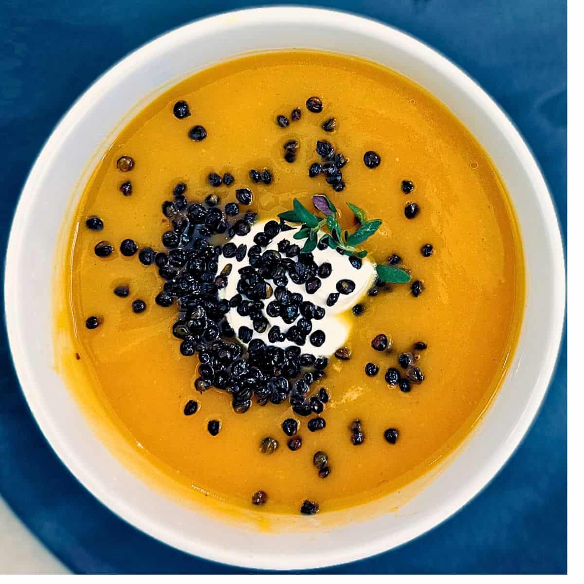 Butternut squash soup in a white bowl on a black plate.