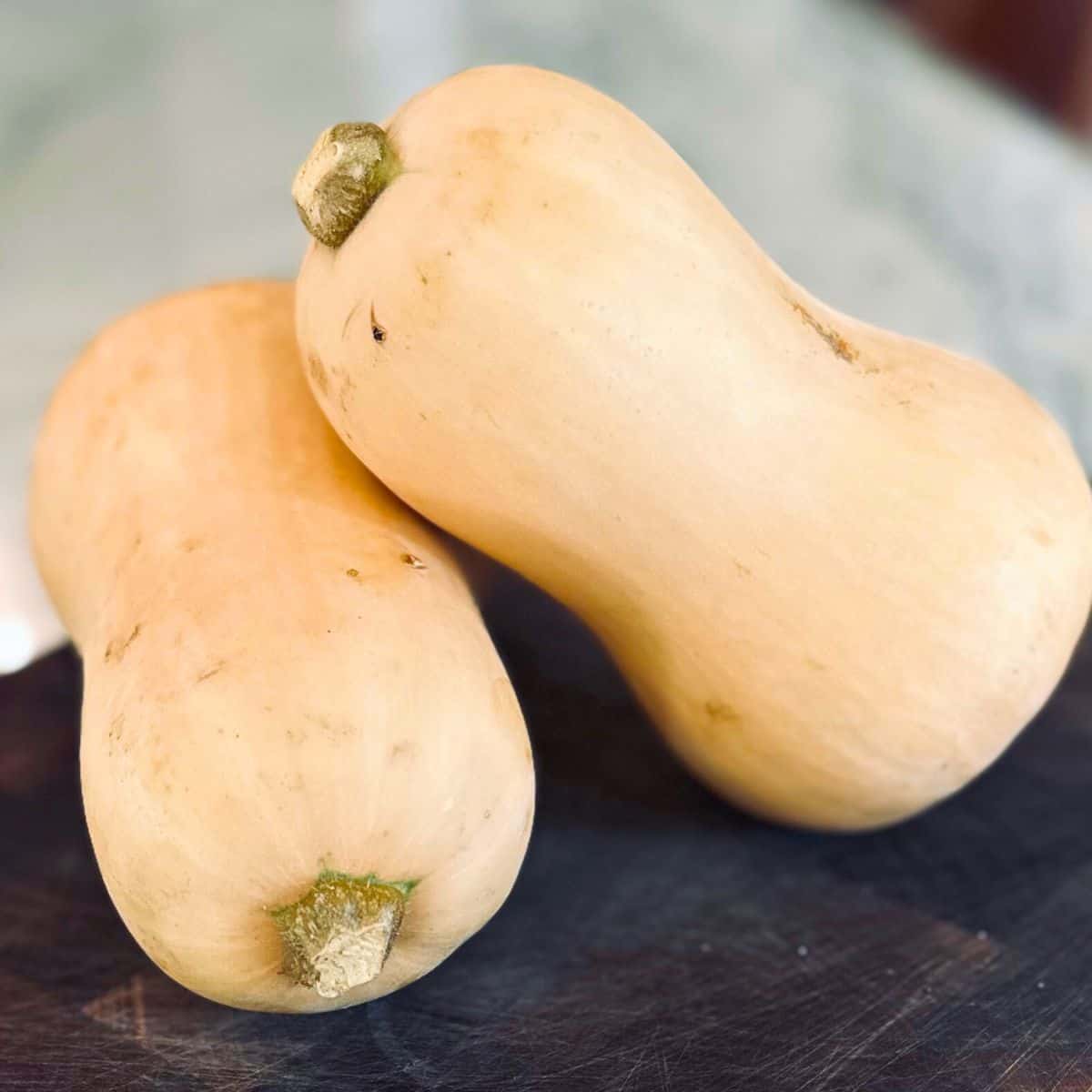 Two butternut squash on a dark cutting board.