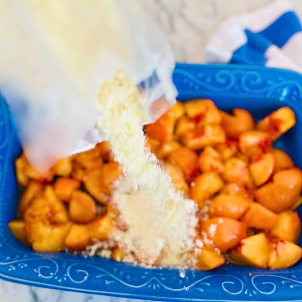 Cake mix being poured over a pan of peaches.