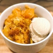 Peach dump cake with ice cream in a white bowl.