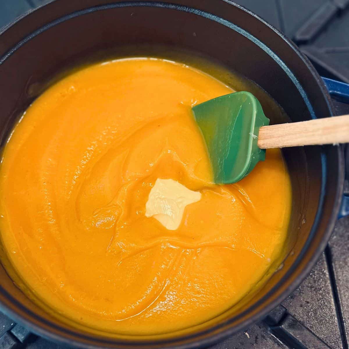 Butternut squash soup in a pot with butter and a green spatula.