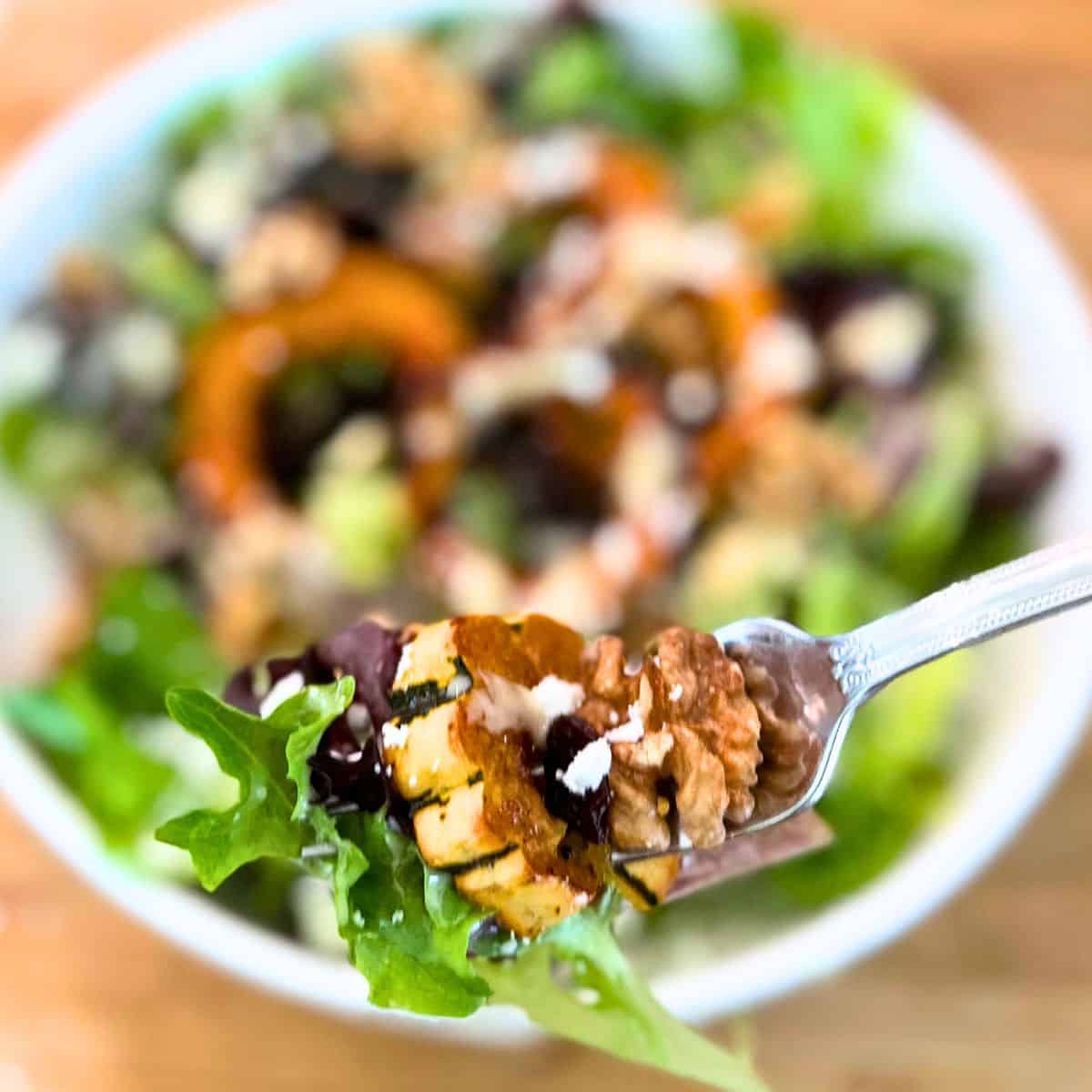 A bite of delicata squash salad on a fork with the salad in the backgroud.