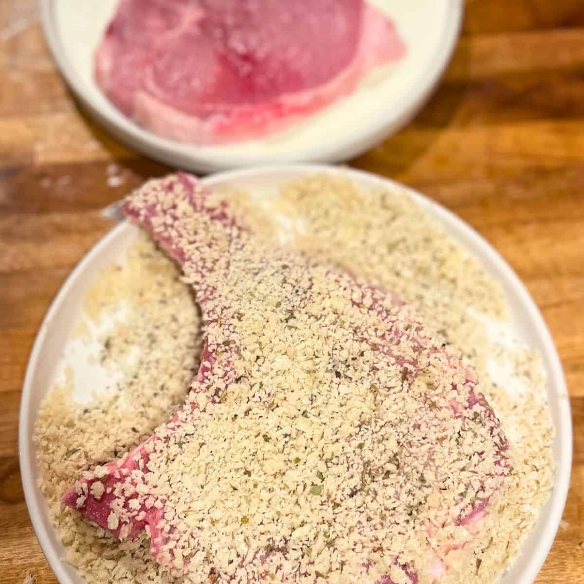 Raw panko crusted pork chop on a white plate.