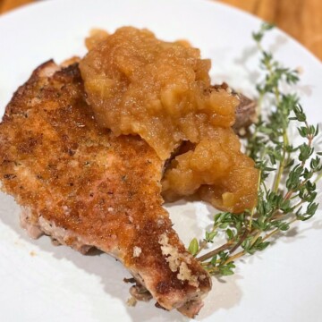 Pork chop and applesauce with thyme on a white plate.