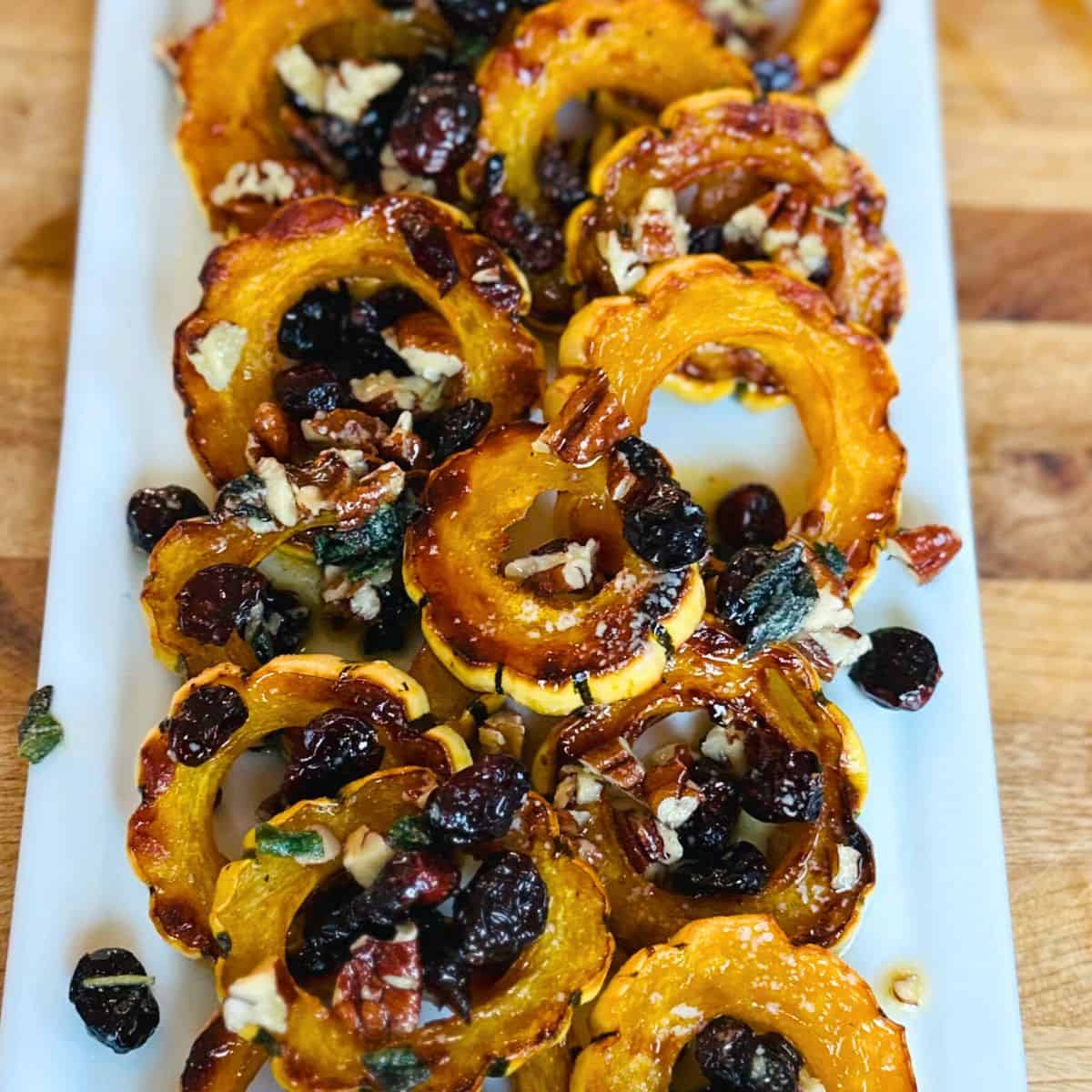 Roasted delicata squash with cranberries and pecans on a white platter.